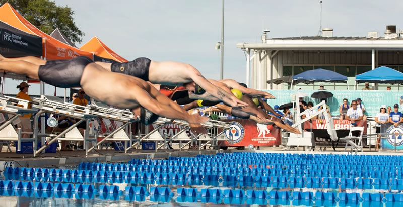 Male swimmers diving from starting blocks during a Minutes to Seconds comparison of Olympic race times